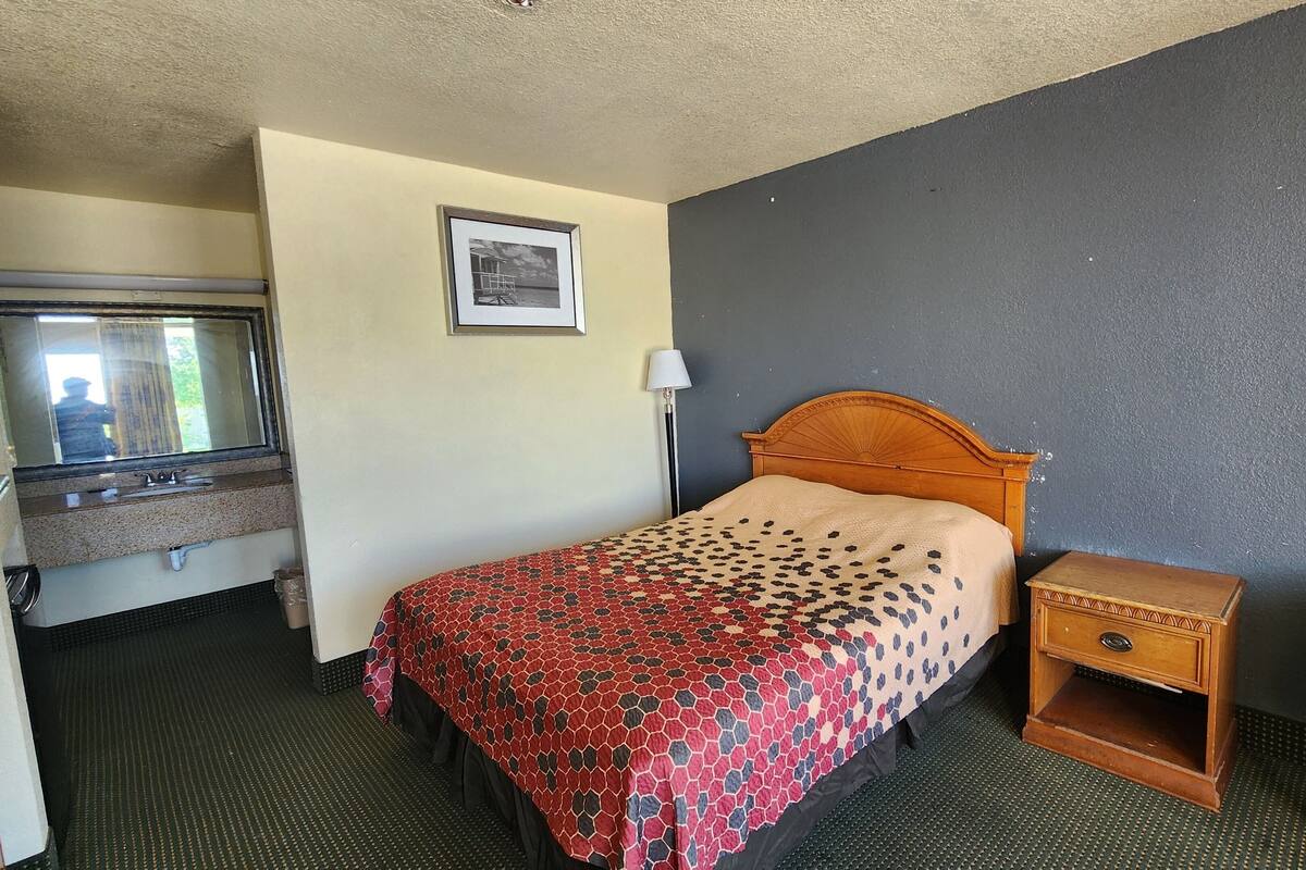Habitación de hotel con cama, mesita de noche, silla, espejo y un cuadro en la pared.