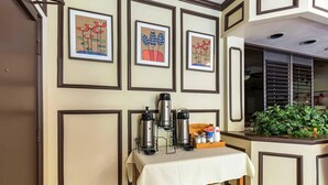 Ein Hotelzimmer mit gedecktem Frühstückstisch, gerahmten Kunstwerken an den Wänden und Blick auf den Garten durch das Fenster.