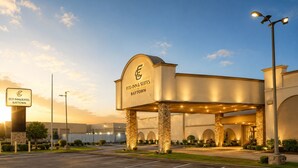 Ein Hotel Eingang mit einem großen Schild, auf dem 'ECO INN & SUITES BAYTOWN' steht, ein Parkplatz und ein klarer Himmel.