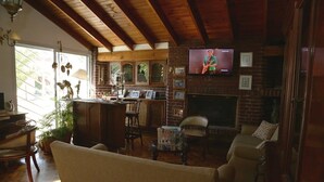 A cozy living room with a fireplace, wooden ceiling, and a television mounted on the wall. - Posada Bernies (Ezeiza)