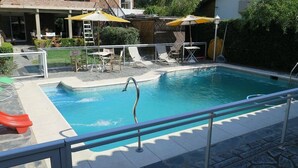 A swimming pool with a metal safety railing, lounge chairs, and umbrellas. - Posada Bernies (Ezeiza)
