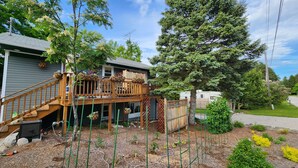 Un immobile residenziale con una terrazza in legno, un giardino recintato e un grande albero.