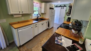 Una cucina compatta con mobili bianchi, lavastoviglie, frigorifero e piano cottura.