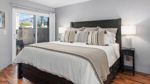 A bedroom with a large bed, two bedside lamps, and a view through a sliding door to an outdoor area. - Casas Adobes Summer Townhouse | Pool & Hot Tub (Tucson)