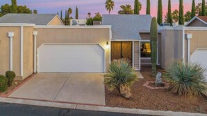 A residential house with a garage, a well-maintained garden with yucca plants, and tall cypress trees in the background. - Casas Adobes Summer Townhouse | Pool & Hot Tub (Tucson)