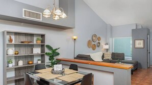 A modern kitchen with a dining area, featuring a central island, built-in shelving, and a grey color scheme. - Casas Adobes Summer Townhouse | Pool & Hot Tub (Tucson)