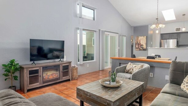 A modern living room with a flat-screen TV, grey sofas, a wooden coffee table, and a fireplace. - Casas Adobes Summer Townhouse | Pool & Hot Tub (Tucson)