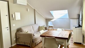 Et værelse med sofa, spisebord, stole, fjernsyn og ovenlys.