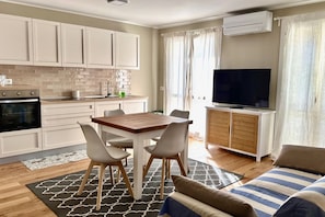 A modern kitchen with white cabinets, a dining table with chairs, a flat-screen TV, and a sofa with striped cushions. - P016 - Porto Recanati, new three-room penthouse 30m from the sea (Porto Recanati)