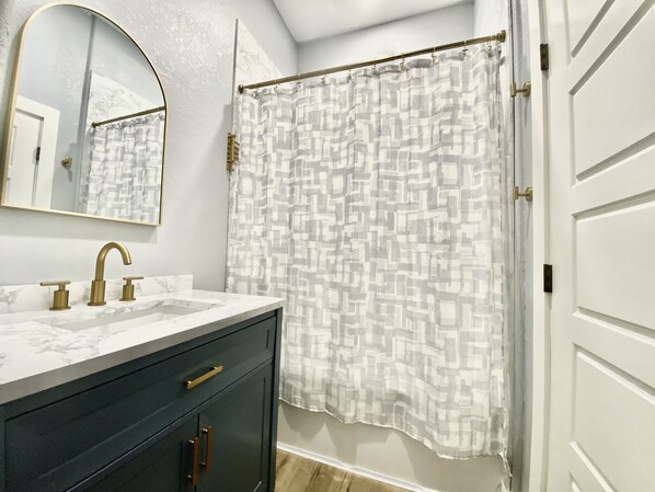 A bathroom with a marble sink, a dark cabinet, a shower curtain with a geometric pattern, and a white door.
