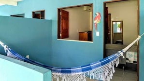 A room with a hammock, a wooden door, and a mirror reflecting a room with a bed. - Pousada Tulum (Maraú)