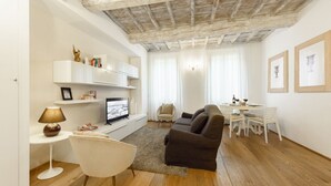 A living room with a sofa, TV, white chair, and a dining table with chairs. - Don Giovanni apartment in Florence by Mmega (Florence)