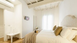 A bedroom with a bed, a bench, a radiator, a TV, and a window with curtains. - Don Giovanni apartment in Florence by Mmega (Florence)