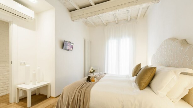 A bedroom with a bed, a bench, a radiator, a TV, and a window with curtains. - Don Giovanni apartment in Florence by Mmega (Florence)