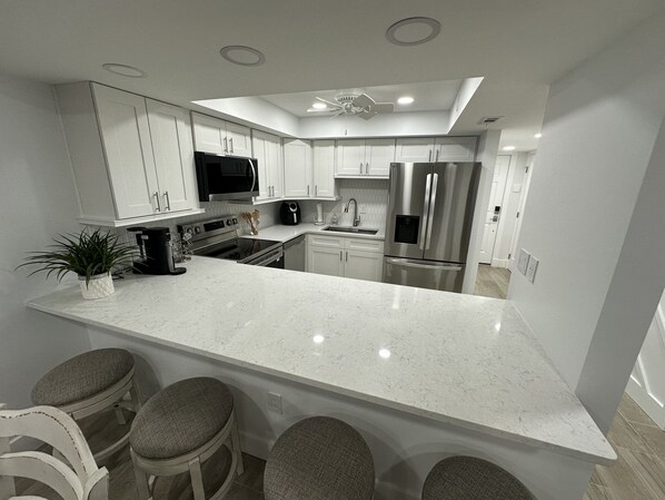 Een moderne keuken met witte kasten, roestvrijstalen apparatuur, een groot eiland met barstoelen en inbouwspots.