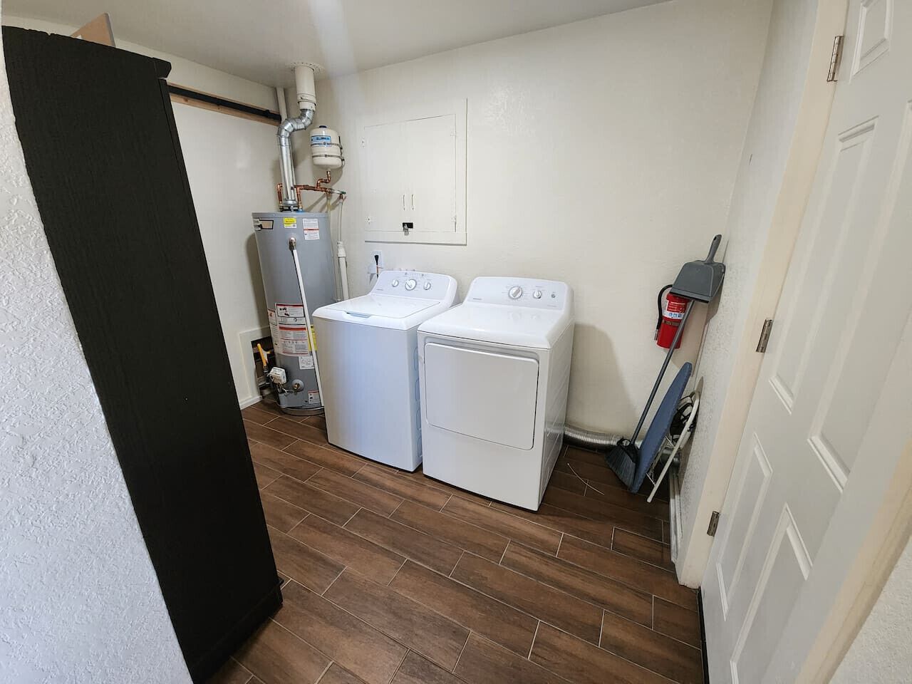 A laundry room with two washing machines, a water heater, and a broom.