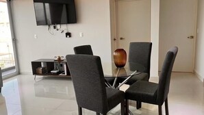 A modern dining area with a glass table, four chairs, a flat-screen TV mounted on the wall, and a minimalist design. - Departamento a 20 metros de 5a Av. (Playa del Carmen)