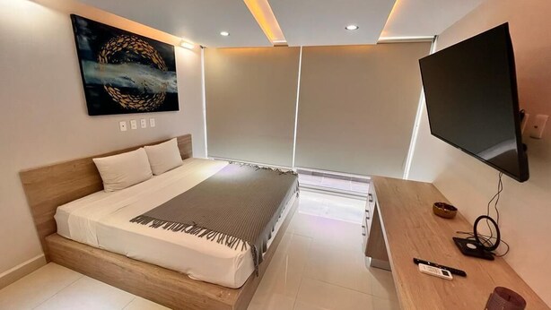 A modern bedroom with a bed, bedside table, TV, and artwork. - Departamento a 20 metros de 5a Av. (Playa del Carmen)