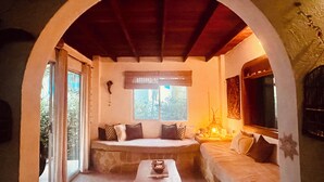 Una habitación acogedora con un banco de piedra, una mesa de madera y una zona de estar con cojines bajo un techo abovedado.