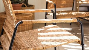 A wicker chair and a table in a room with large windows and potted plants.