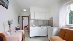 A compact kitchen with white cabinets, a dining table with chairs, and a sofa. - Holiday apartment with air conditioning (Rabac)