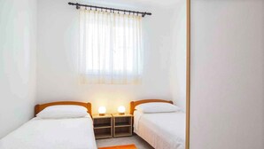 Une petite chambre propre, avec deux lits simples, une fenêtre ornée de rideaux légers et des lampes de chevet.