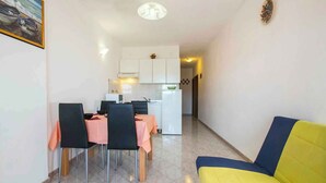Un coin repas avec une table dressée pour quatre personnes, un canapé jaune et une cuisine en arrière-plan.