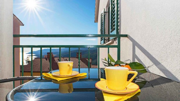 A balcony with a glass table, two yellow cups, and a green railing. - Holiday apartment with air conditioning (Rabac)
