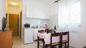 A compact kitchen with white cabinets, a microwave, and a dining table set with chairs. - Holiday apartment with air conditioning (Rabac)