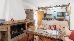 A cozy living room with a fireplace, a glass coffee table, and a sofa with floral cushions. - Tere 2 Antequera - La Higuera by Ruralidays (Málaga)