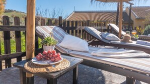 A sunlit outdoor seating area with lounge chairs, a table with a plate of grapes and a succulent plant, and a wooden fence in the background. - Tere 2 Antequera - La Higuera by Ruralidays (Málaga)