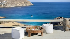A seaside terrace with a wooden table set for breakfast, overlooking a clear blue sea and a rocky coastline. - Villa Magnolia  (Mykonos)