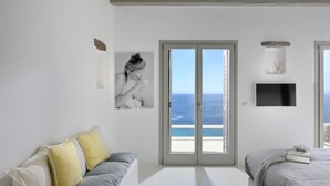 A bedroom with a large window, a bed, a sofa, and a TV. - Villa Magnolia  (Mykonos)
