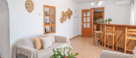 A cozy living room with a sofa, a dining table with chairs, and a kitchen area visible through an open door.