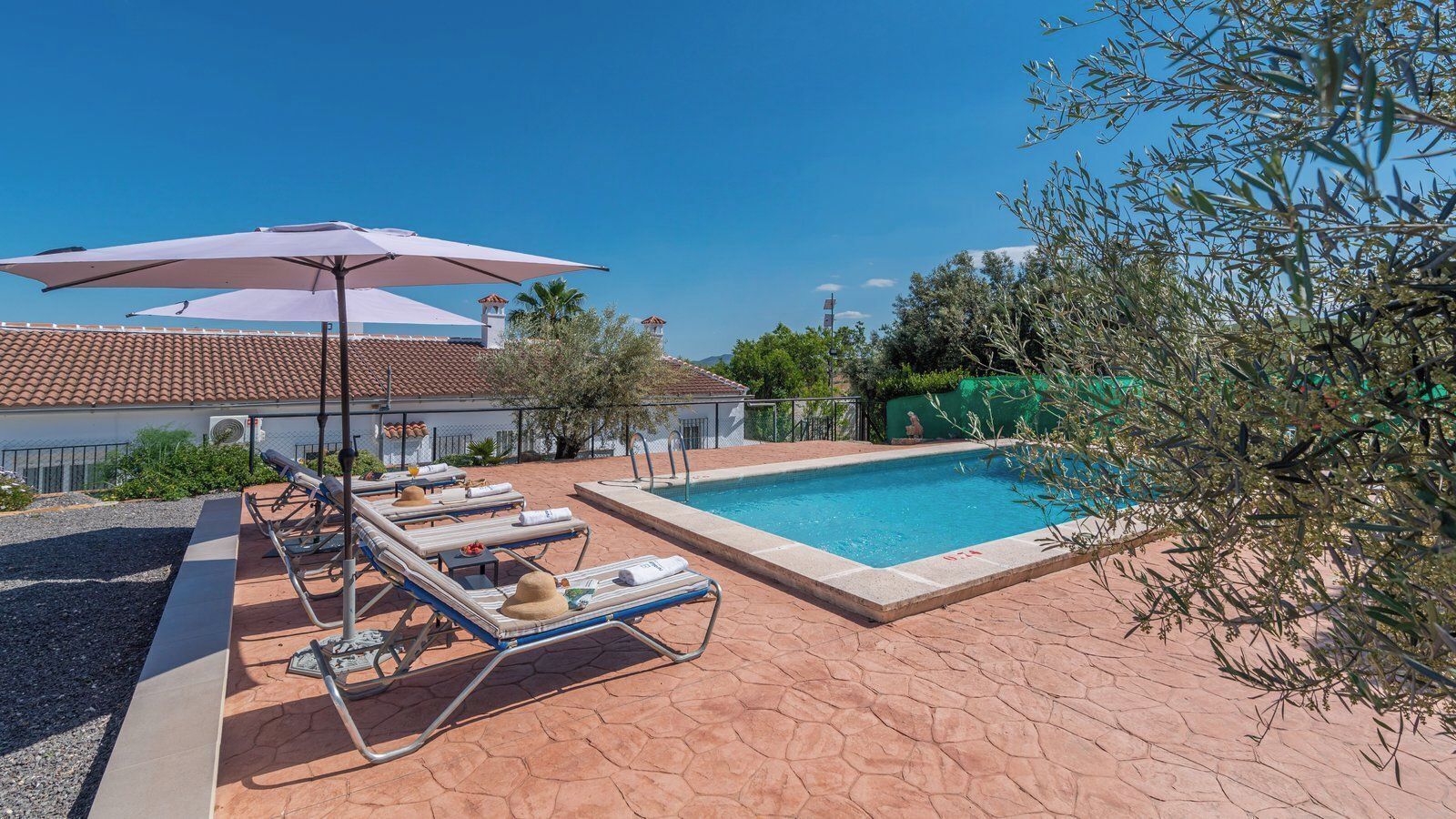 A pool area with lounge chairs and umbrellas, a swimming pool, and a building with a tiled roof.