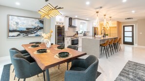 A modern kitchen with white cabinets, a wooden dining table, and a large painting on the wall. - Modern Delray Beach Charmer - Near Atlantic Ave. in Delray Beach (Delray Beach)