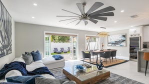 A modern living room with a glass coffee table, a ceiling fan, and a dining area with a table and chairs. - Modern Delray Beach Charmer - Near Atlantic Ave. in Delray Beach (Delray Beach)