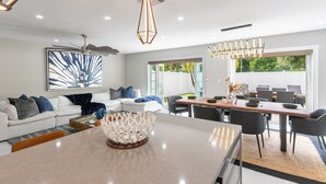 A modern living room with a white sofa, a dining area with a wooden table, and a large window providing a view of the outdoors. - Modern Delray Beach Charmer - Near Atlantic Ave. in Delray Beach (Delray Beach)
