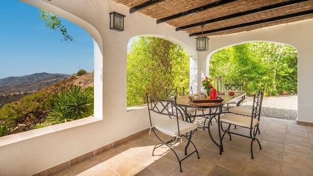 A covered patio with a round table and chairs, surrounded by white walls and large windows. - Las Adelfas Cómpeta by Ruralidays (Málaga)