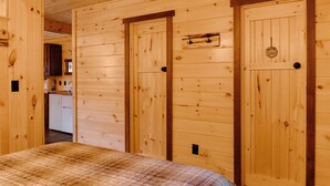 Un intérieur en bois avec un lit, deux portes et, au fond, un coin cuisine.