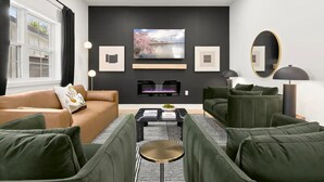 A modern living room with a fireplace, green sofas, a coffee table, and artwork on the walls. - King Beds <> A Sumptuously Lavish Suite Xcape (Alexandria)