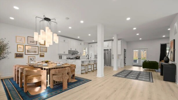 A modern kitchen with white cabinets, a central island, and a dining area with a round table and chairs. - King Beds <> A Sumptuously Lavish Suite Xcape (Alexandria)