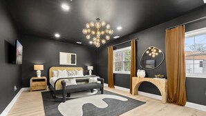 A modern bedroom with a large bed, a chandelier, a fireplace, and a view of the outdoors. - King Beds <> A Sumptuously Lavish Suite Xcape (Alexandria)