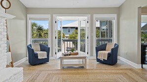 A spacious living room with two blue armchairs, a white coffee table, and a large window offering a view of the outdoors.