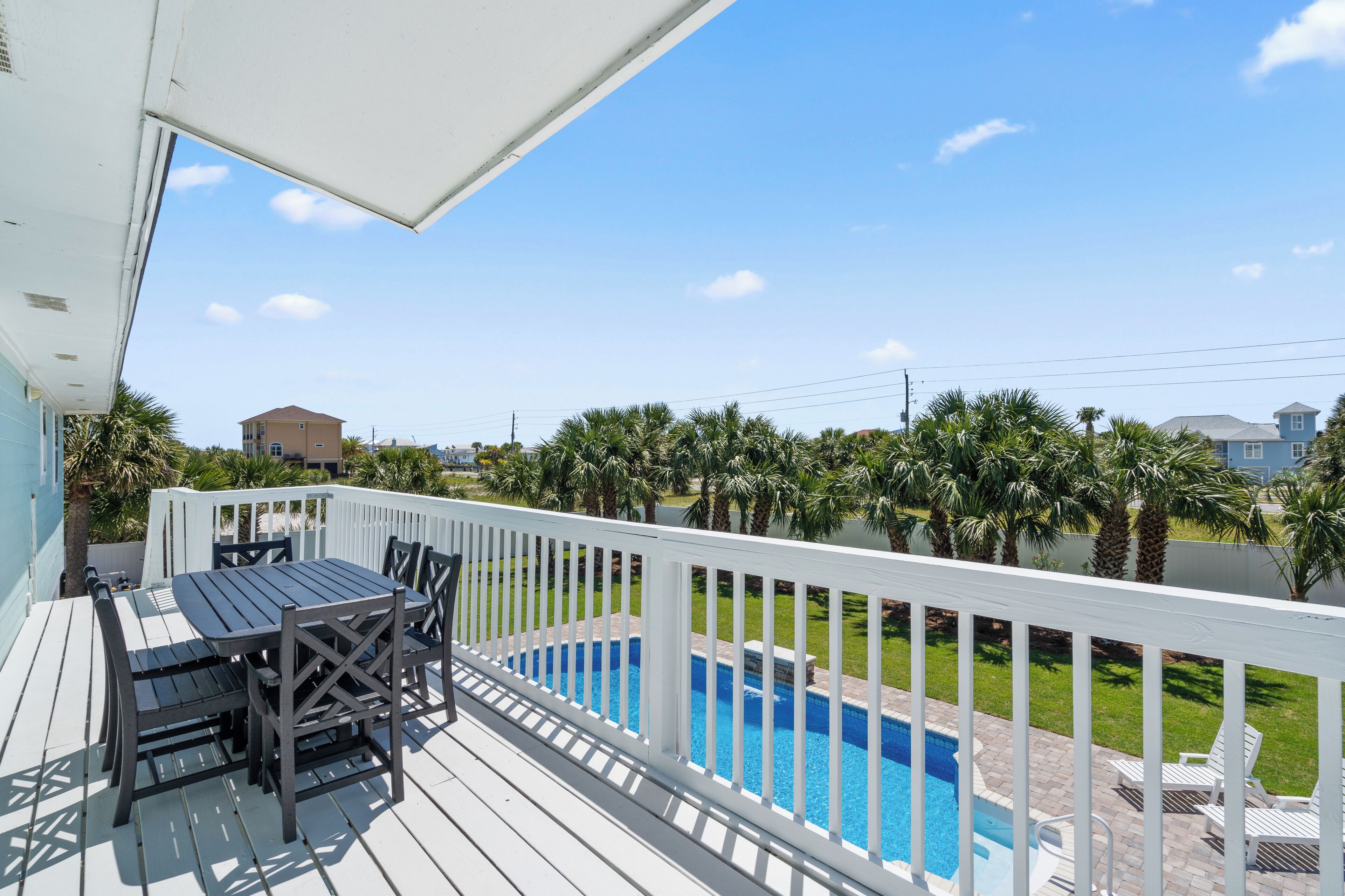 A deck with a pool, white railing, and a table with chairs.