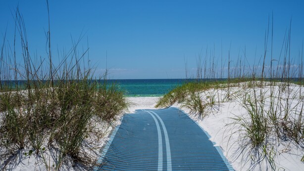 A pathway leading to a beach with white sand and clear blue water.