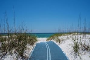 Ein Weg führt zu einem Strand mit weißem Sand und klarem, blauem Wasser.