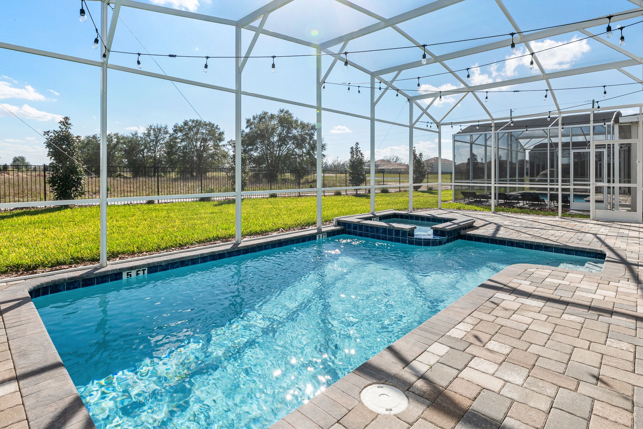 A swimming pool with a glass enclosure, surrounded by a brick patio and a grassy area.