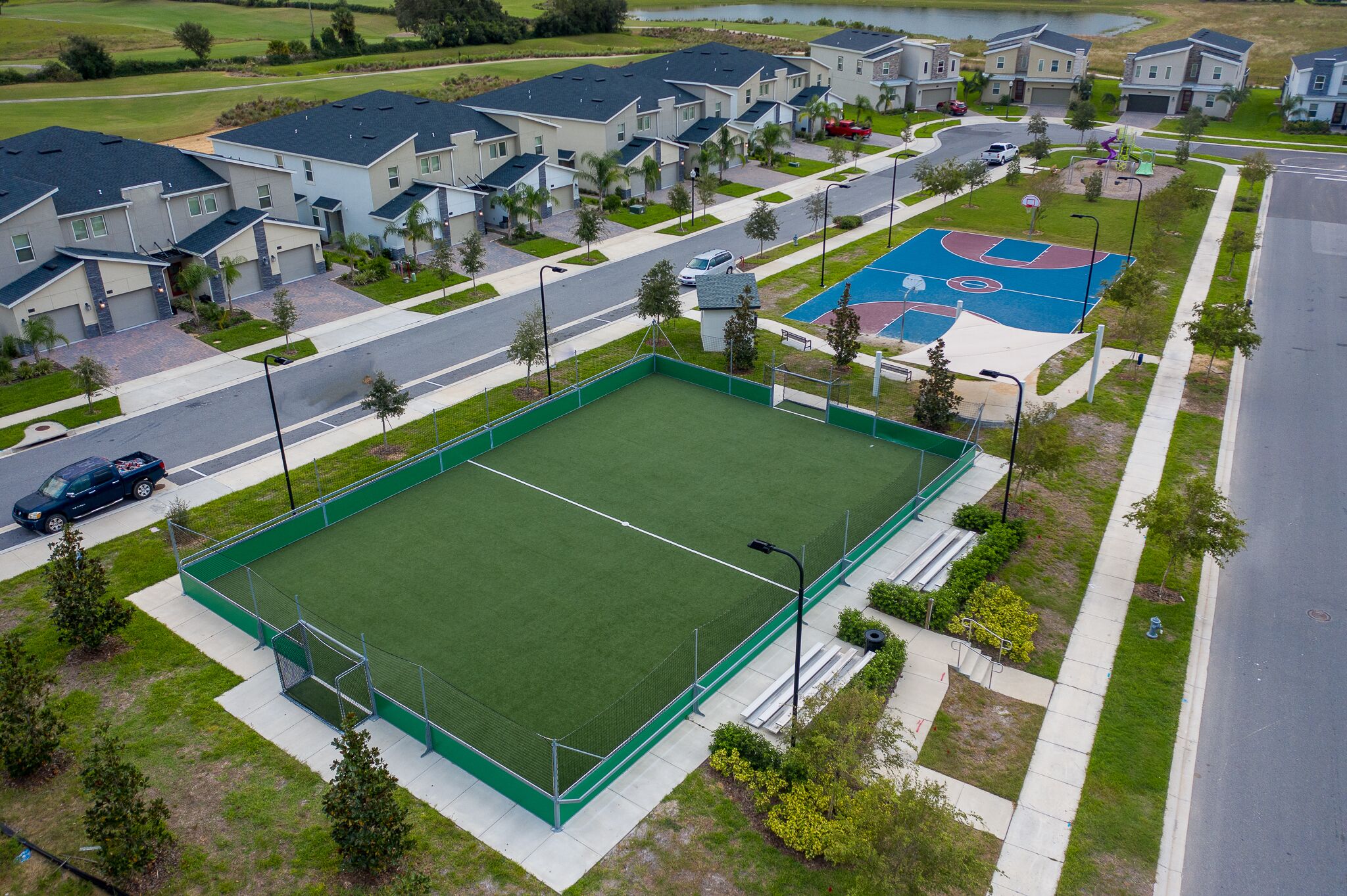 A residential area with modern houses, a basketball court, and a fenced sports field.