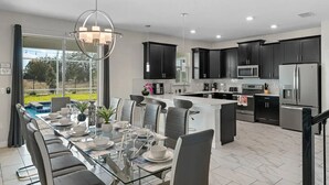 Una cocina moderna con armarios oscuros, electrodomésticos de acero inoxidable y un comedor con mesa y sillas de vidrio.